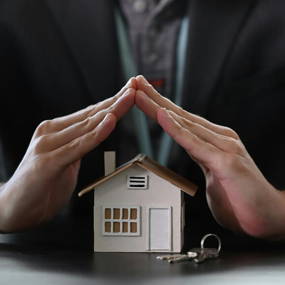 Photo d'illustration montrant une petite maison mise à l'abri par deux mains mimant un toit plus grand au-dessus d'elle.