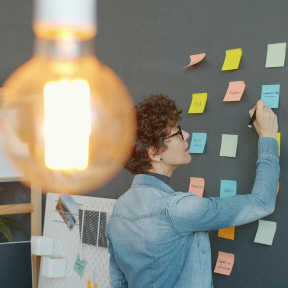 Photo d'illustration : une ampoule lumineuse éclaire un homme en train de noter des idées sur des post-it.